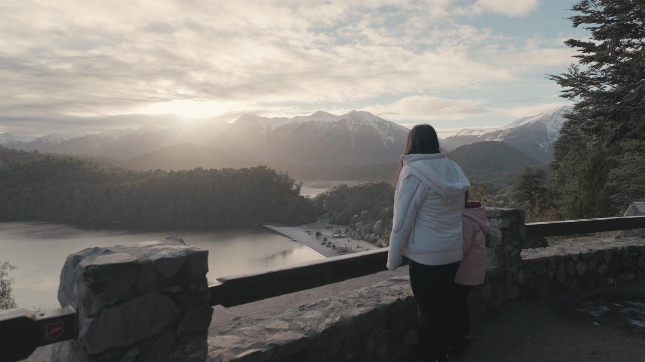 En mor og datter beundrer solopgangen over Lago Espejo, omgivet af sneklædte bjerge. Ideel til familie rejseindhold eller naturdokumentarer.