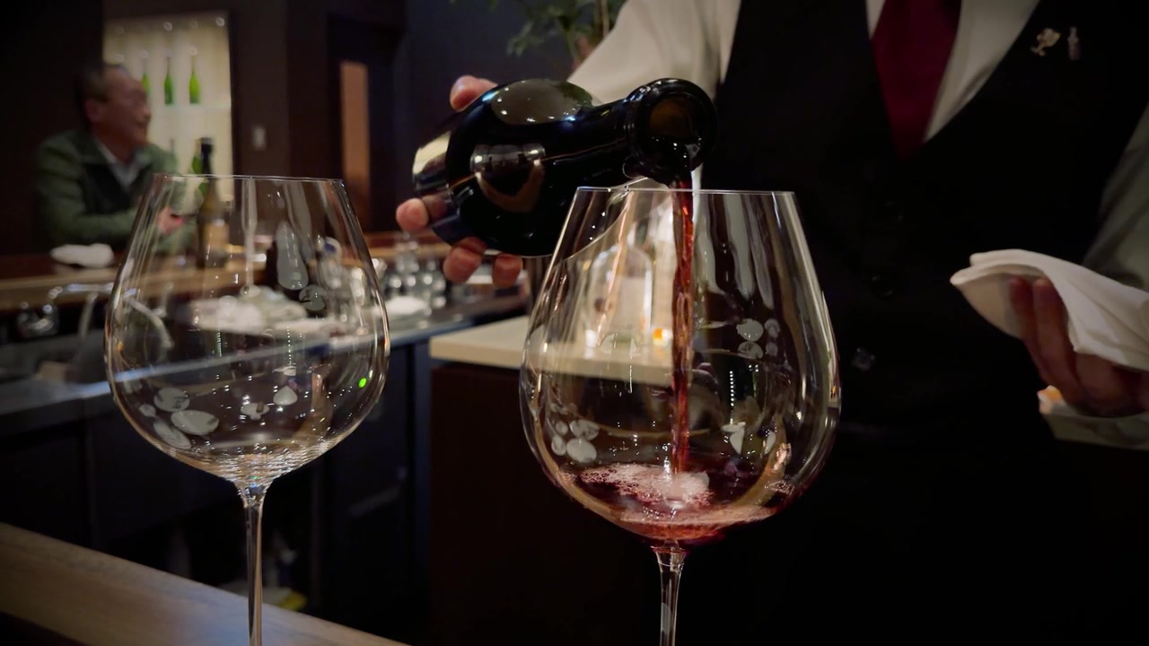 Un sommelier versa vino rosso in un calice di cristallo in un bar giapponese in penombra