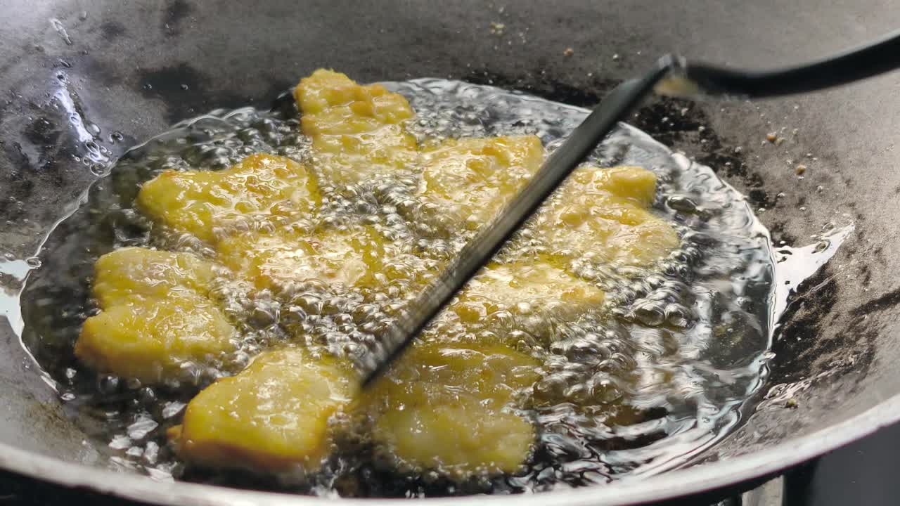 The chef is frying chicken nuggets in a wok. They are using palm oil, and the nuggets sizzle as they cook in the hot cooking oil