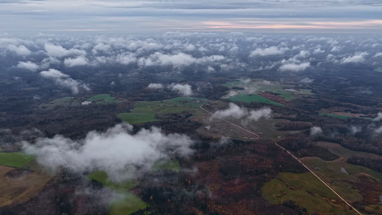 Vista aerea dall'alto che mostra le nuvole riversarsi su un mosaico di terreni agricoli mentre l'atmosfera mattutina cambia silenziosamente