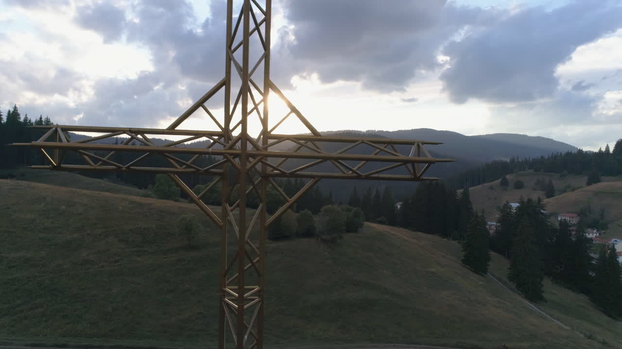AERIAL: Flying around a large metal cross against the backdrop of the sunset