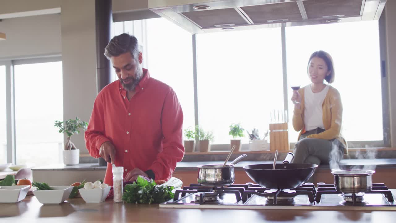 pareja feliz cocinando juntos, cortando verduras y bebiendo vino en la cocina