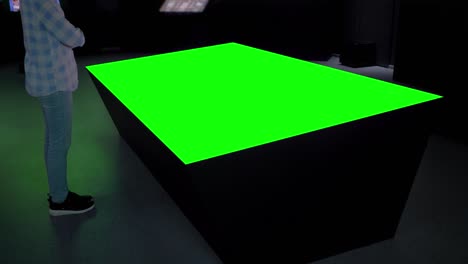 woman looking at blank green display table of table kiosk - green screen concept