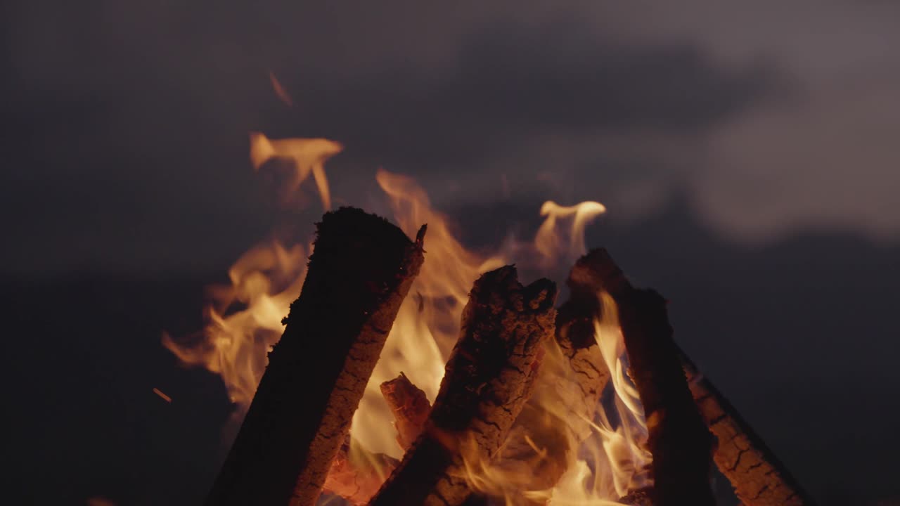 Bright campfire burning in the foreground with a mountain range and lake in the background at night. Peaceful outdoor scene symbolizing warmth, adventure, and solitude in nature