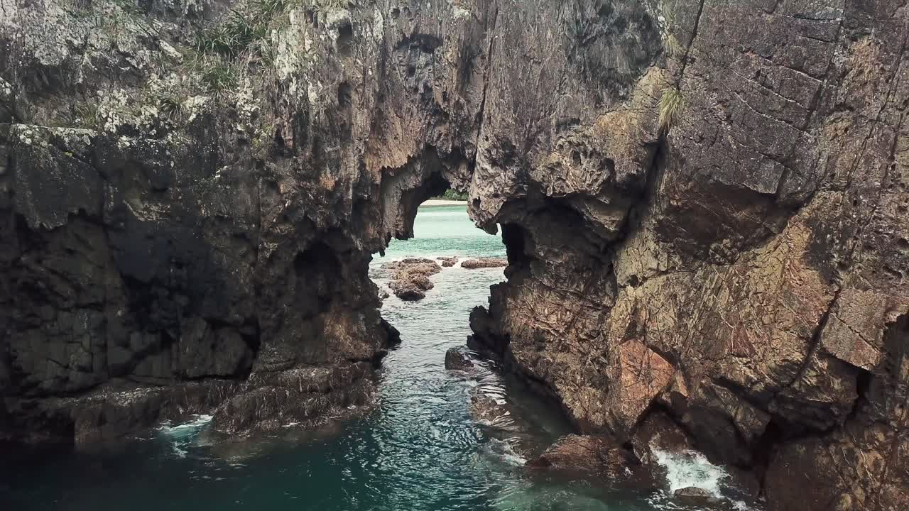 해변 의 바위 에 있는 구 ⁇  을 통해 뒤로 날아가는 드론 - 백인 만 뉴질랜드