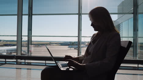 Silhouette-Einer-Geschäftsfrau-Mit-Einem-Laptop,-Der-In-Erwartung-Ihres-Fluges-Arbeitet,-Sitzt-Im-Großen-und-Ganzen