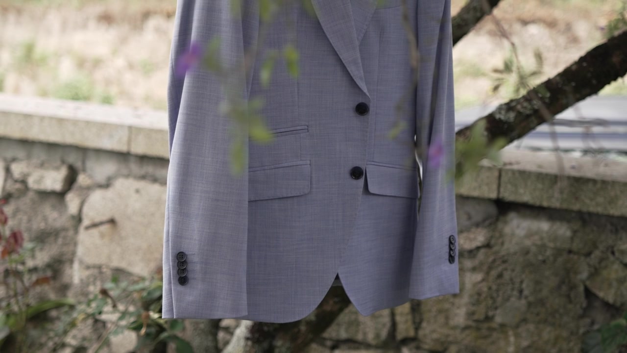 Primo piano di una giacca da completo grigio chiaro appesa all'aperto contro un muro di pietra rustico