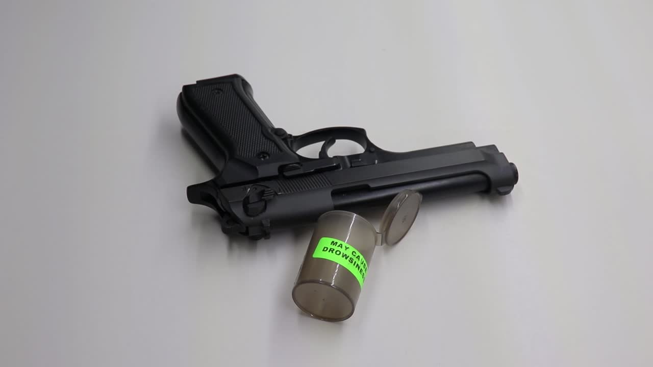 persona vertiendo pastillas para dormir en su mano y luego recogiendo un arma de fuego