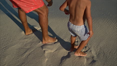 close up of the legs of a young mexican latin boy and his father wearing shorts standing on the sand waiting for a wave in cancun