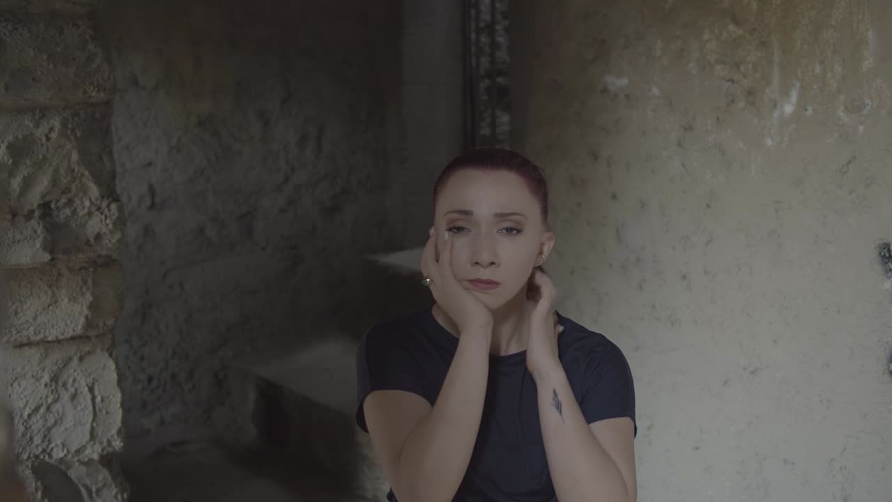 한 젊은 여성이 낡고 어두운 건물에서 감정의 무게로 몸부림치고 있습니다.