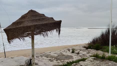 storm-waves-at-beach-shore,-straw-beach-hat-waving-with-strong-winds