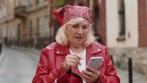 Surprised senior woman use smartphone loses bad news fortune loss fail outdoors in city street