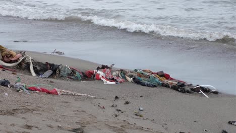 piles of clothes, fabric and textile trash washed ashore from ocean onto beach in tropical island destination in southeast asia, impact of fast fashion industry