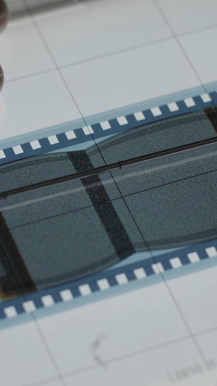 Video verticale: Dita che stringono una pellicola, allineando i fotogrammi su una griglia retroilluminata durante l'ispezione