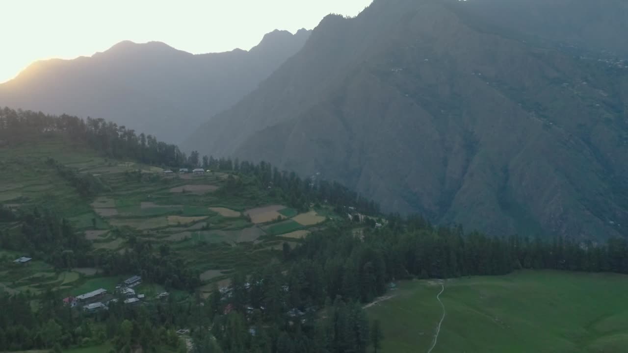 aerial view of a beautiful and offbeat rural mountain valley in asia with grasslands and terrace farm. green and serene. surrounded by tall mountains.  beautiful golden hour footage