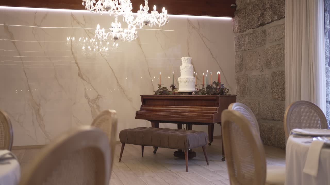 White tiered wedding cake displayed on grand piano under chandelier in luxury stone venue