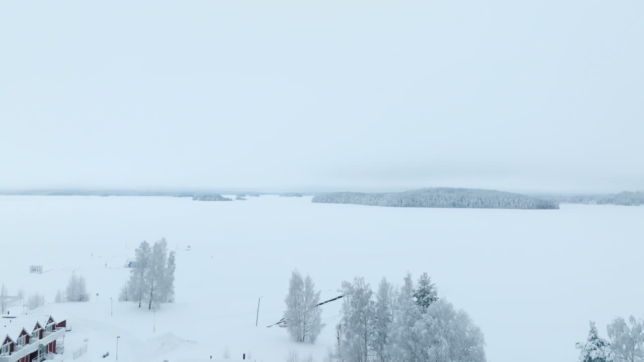 Aerial view through snowy forest, revealing a snowstorm above a lake, winter in Finland