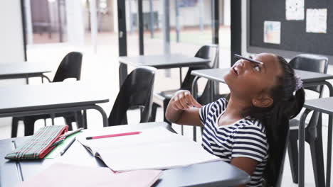 A-young-African-American-girl-sits-at-desk,-pencil-on-her-nose,-copy-space