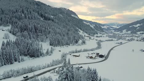 Aerial-shot-of-a-snow-covered-mountain-town,-winding-road-through-the-valley