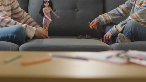 close up of two children playing with gender specific doll and dinosaur toys at home