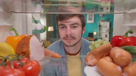 man looking inside a full refrigerator