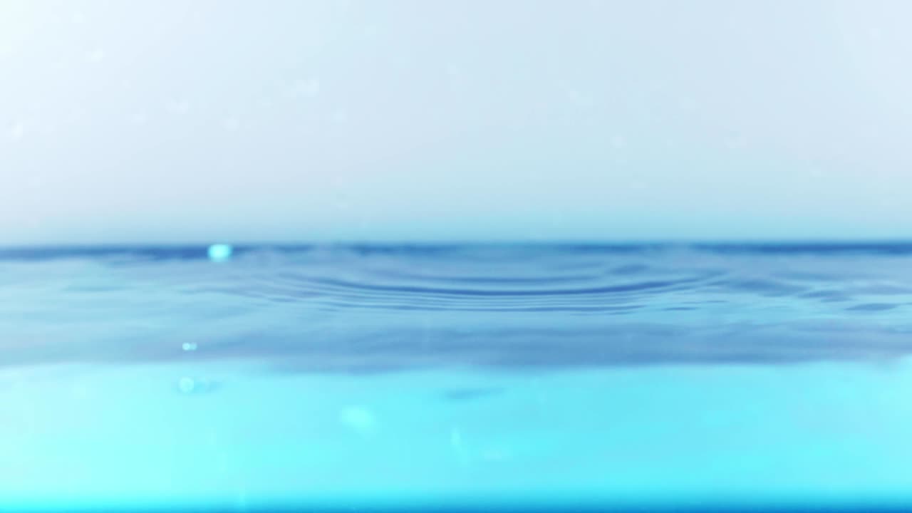 슬로우 모션의 깨끗한 물 표면은 물이 튀는 상점으로 화면을 채우고 기포로 액체 표면을 흔들고 있습니다.