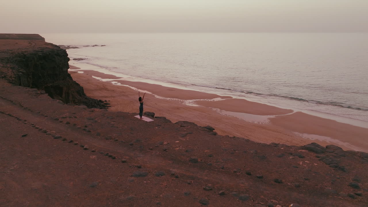Woman practicing yoga on a beach cliff at sunrise/sunset