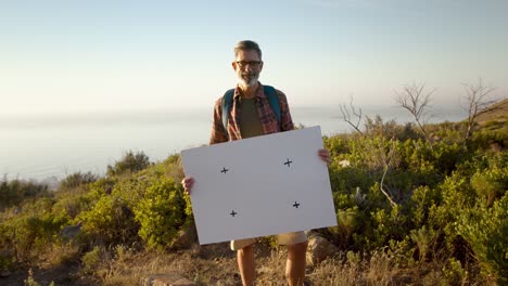 mature hiker holding a blank placard on a hilltop