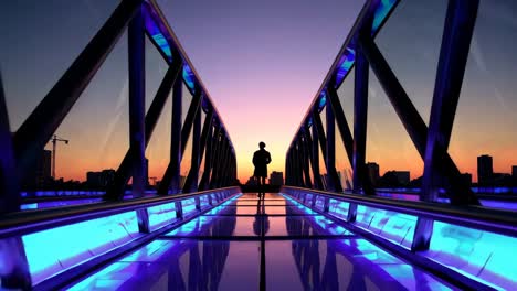 silueta de una persona en un puente de vidrio moderno al atardecer