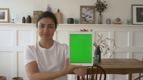 young indian girl smiling looking at the camera holding a tablet with a green screen, showing a new app. bright and cozy room at home. home education learning to know and finance