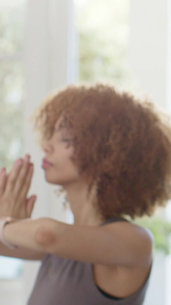 Vertical video: Starting meditation, woman raising prayer hands in tank by tall windows with watch