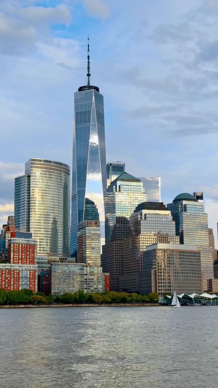 One World Trade Center tårn reflekterer aftensol New York. Vertikalt billede af One World Trade Center og bygninger i Lower Manhattan, der reflekterer gyldent lys fra vandet