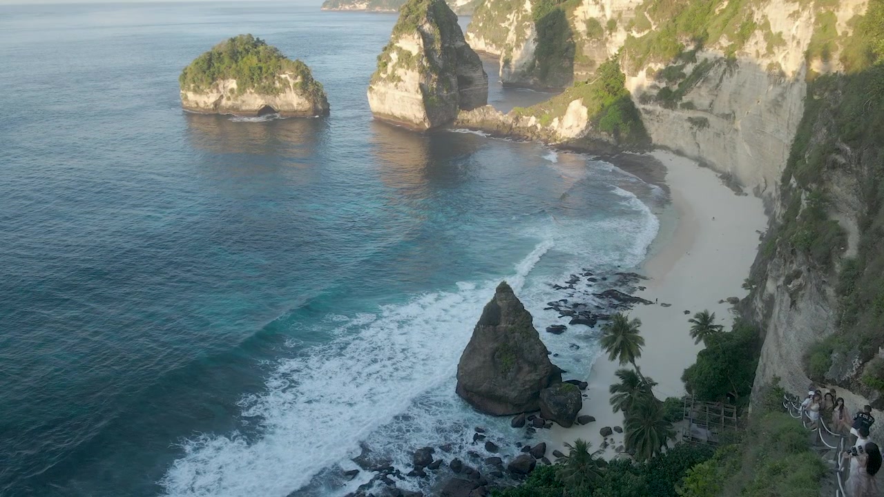 Perspectiva aérea cinematográfica da icônica Diamond Beach em Nusa Penida, Bali, apresentando águas turquesa, areia branca e falésias de calcário durante um pôr do sol quente