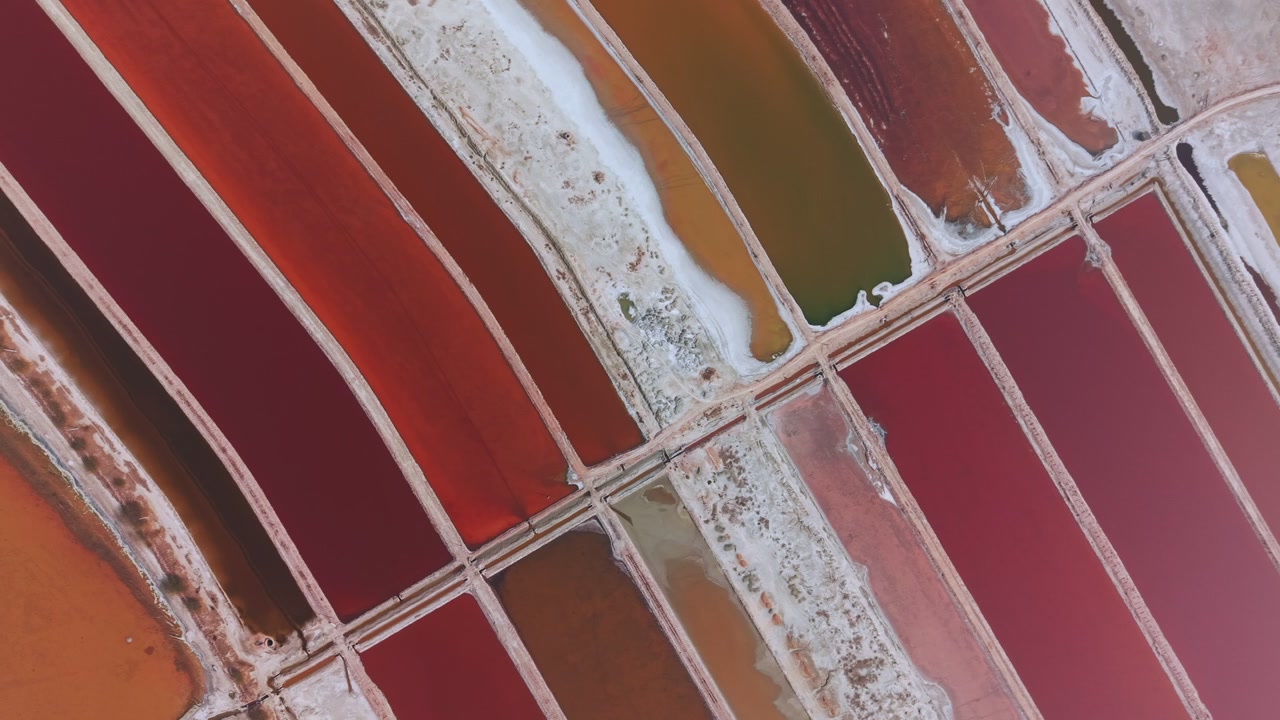 Kolam penguapan di Danau Garam Sambhar menampilkan nuansa merah dan oranye yang dipisahkan oleh jalur-jalur berlapis kerak garam putih. Foto udara ini memperlihatkan pola kisi geometris dari danau garam pedalaman terbesar di India.