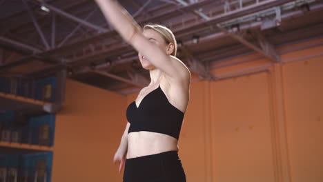 deportista rubia sonriente calentando y estirando su cuerpo en una instalación deportiva cubierta