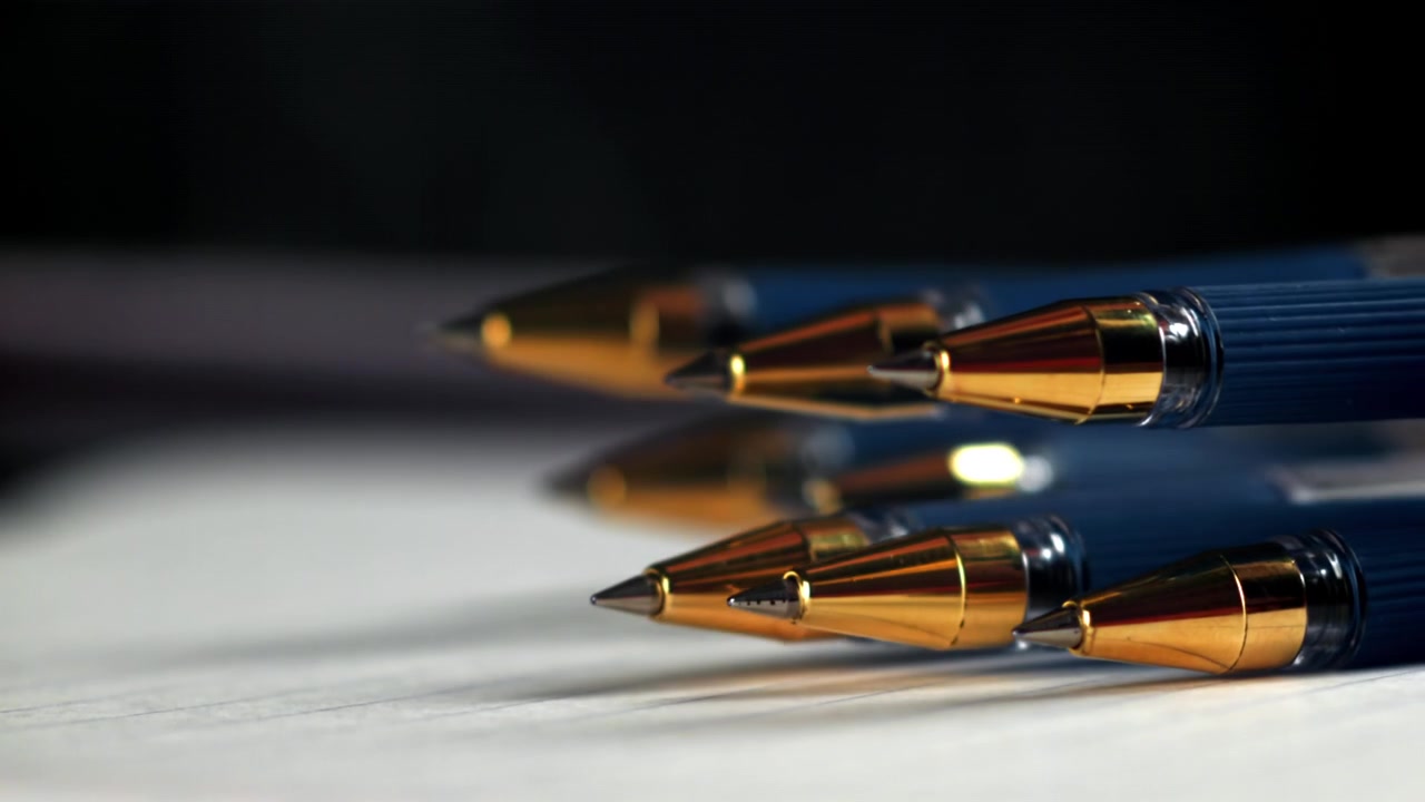 Close-up of Blue Pens with Golden Tips Dropping onto Lined Paper