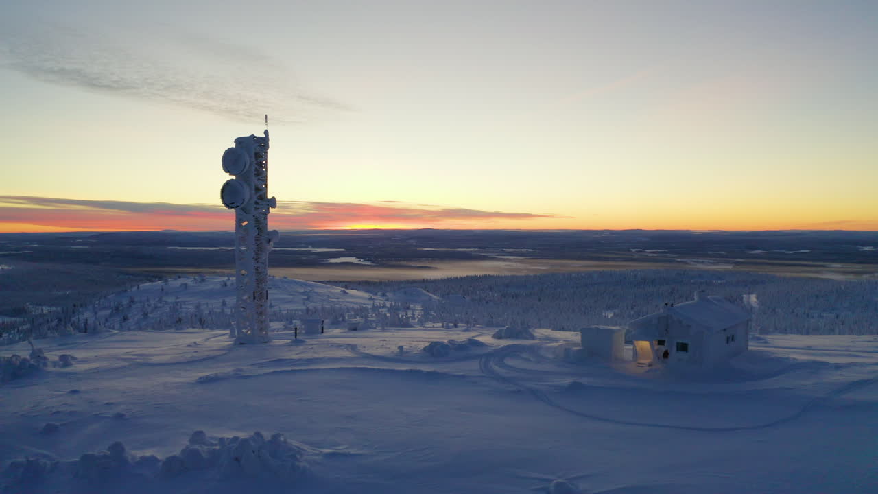 Aerial view moving towards sunrise remote Nordic Lapland cabin and communications tower in polar snow covered wilderness