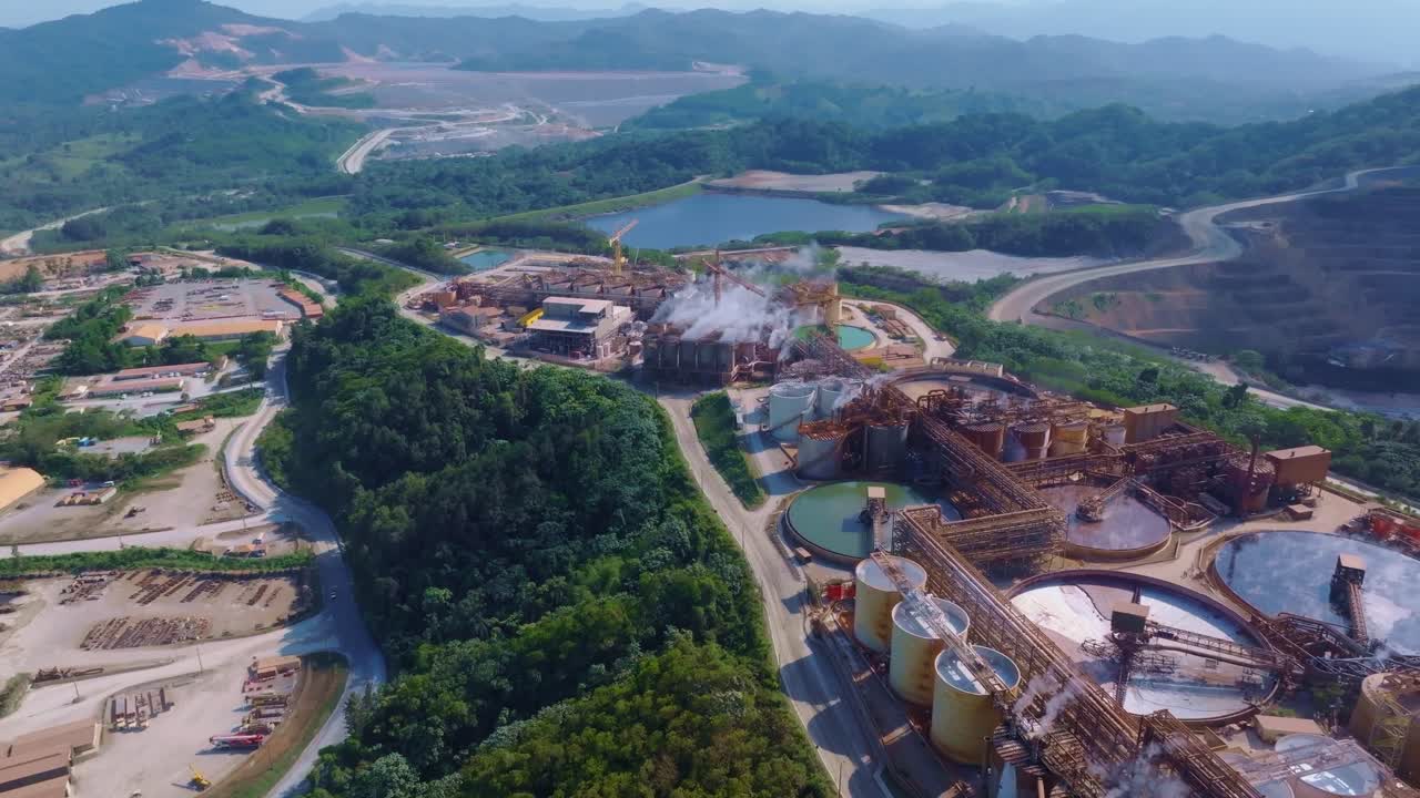 Industrial gold and silver processing complex operated by Barrick Gold, with tanks, steam vents, and supporting infrastructure surrounded by lush hills near Cotuí, Dominican Republic.