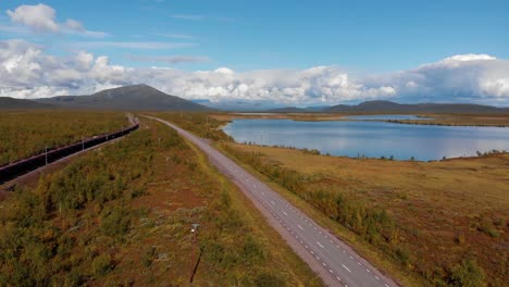 Aerial:-ore-train-in-Kiruna,-Sweden-by-a-main-and-deserted-road-among-forests-and-lakes