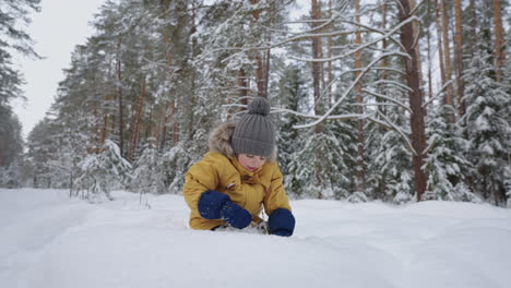 a boy in a yellow jacket takes out a blade of grass and examines studying the winter forest winter walks and through the snowy forest in slow motion. the concept of a free environment for children