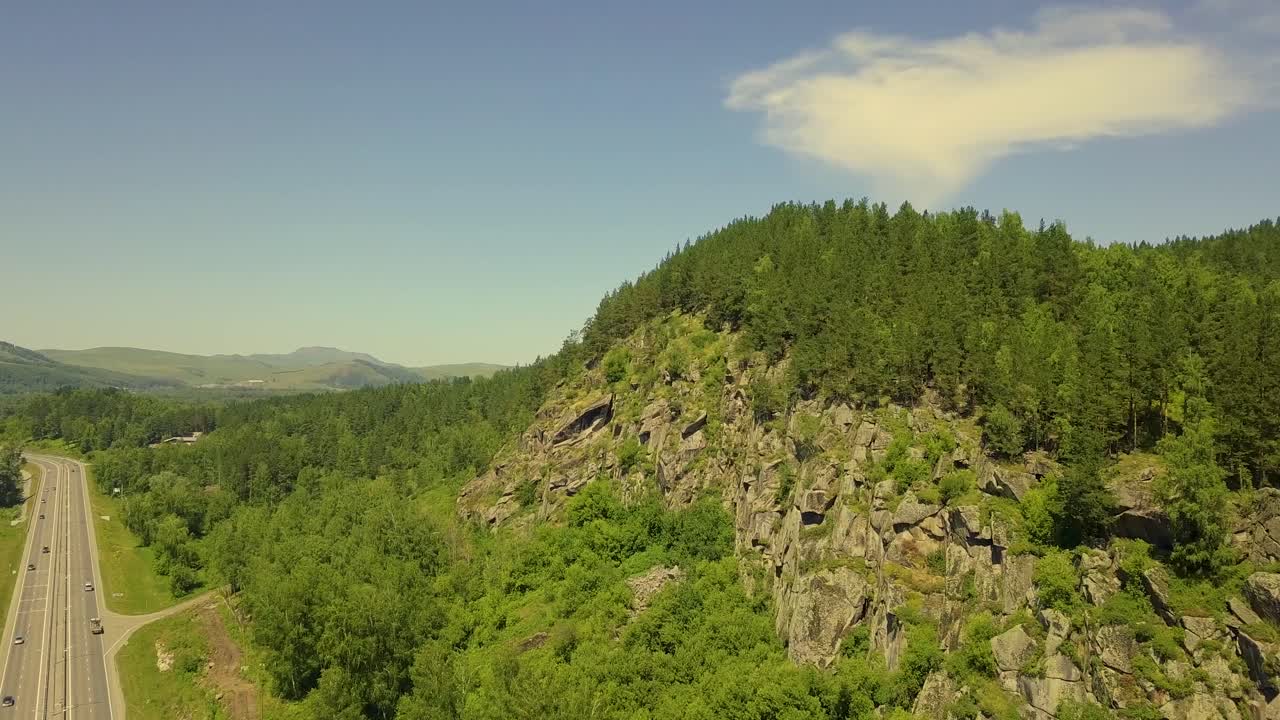 avión volando a lo largo de la montaña de piedra con un bosque de coníferas por debajo - la carretera conduciendo coches