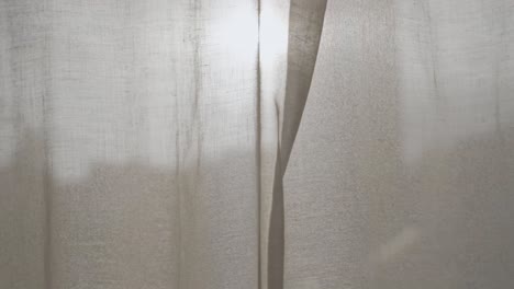 male hand opens window curtain or drape to reveal sunset or sunrise outdoors. man moves fabric to show the light of day outside in city or urban view. warm sunlight shining in creating artistic flare