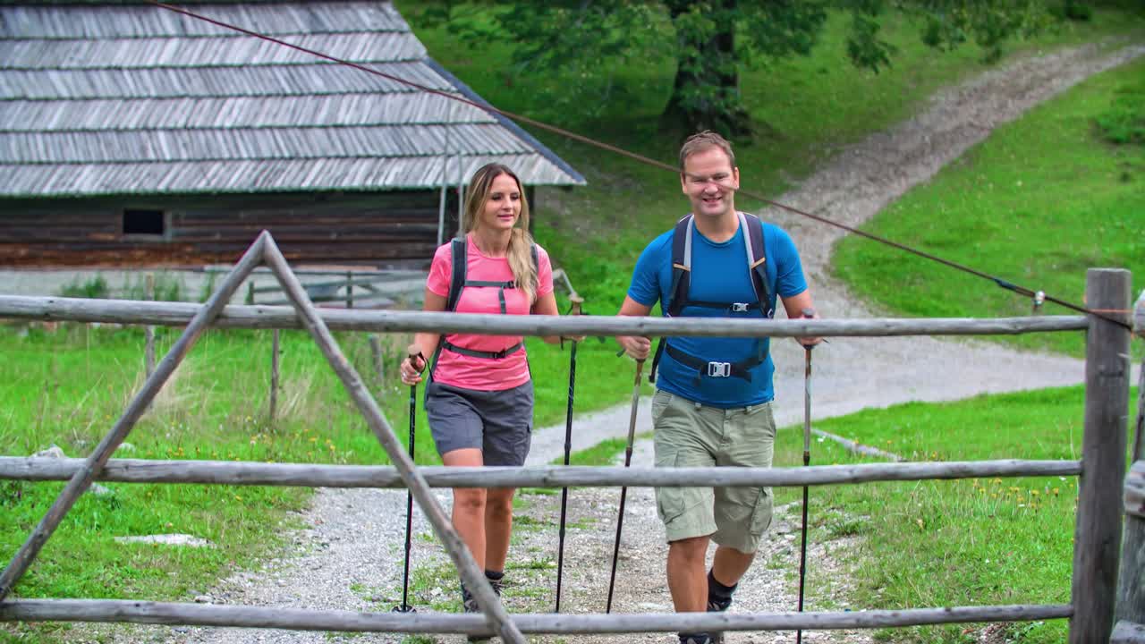 An active couple opening a fence and leaving their wooden hut accommodation to hike in the woods