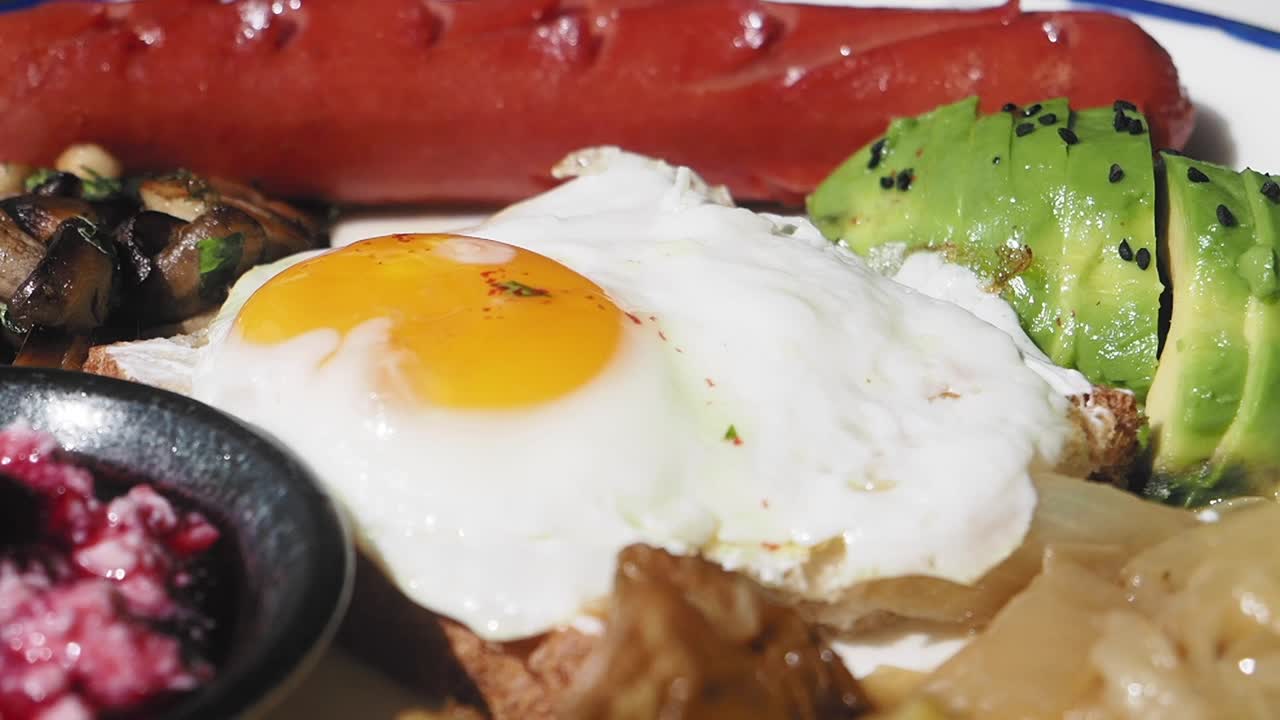 Close-up of a delicious breakfast plate with fried egg, avocado, and sausage