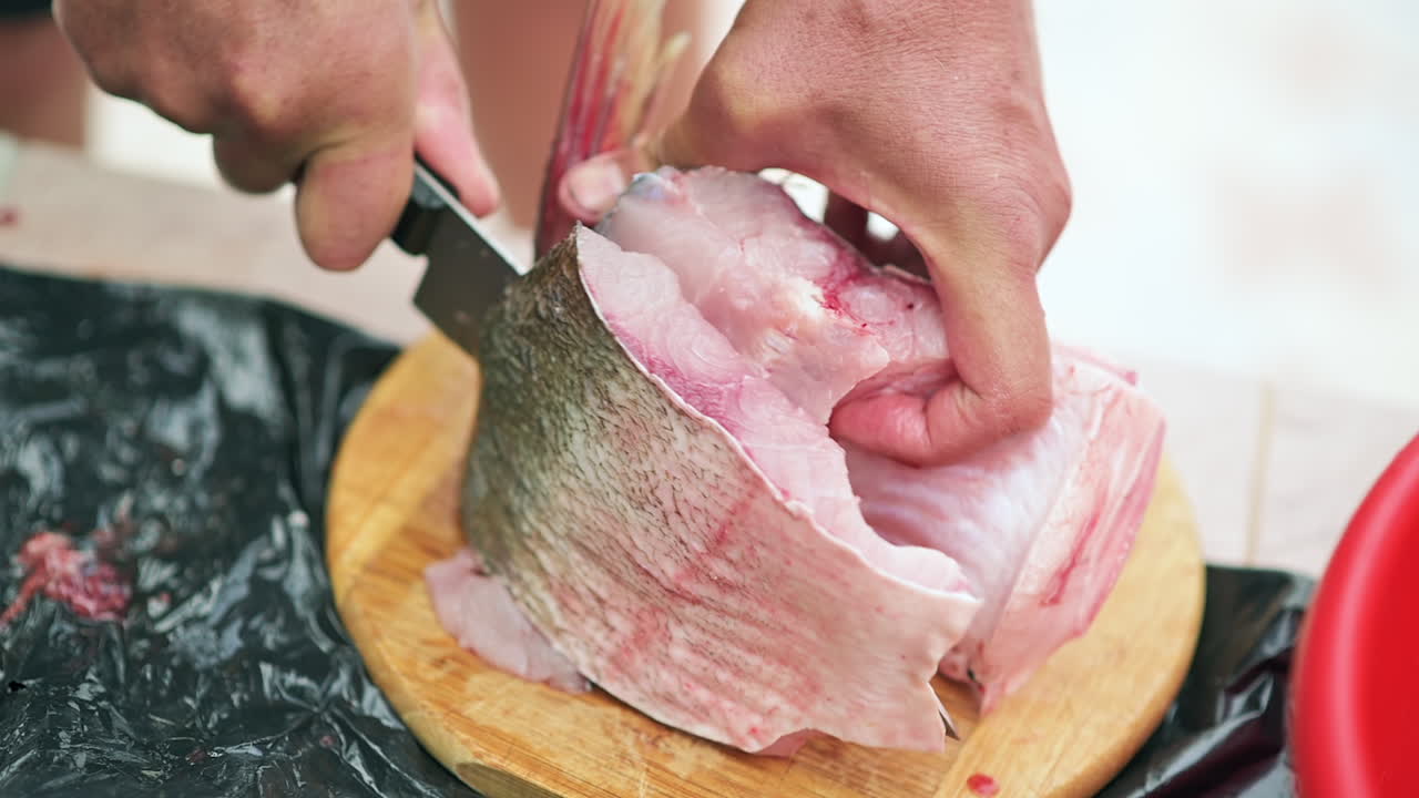 Close up of a man slicing a fish fillet on a wooden cutting board