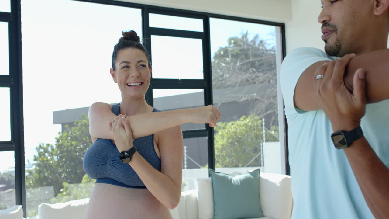 Stretching together, pregnant woman and man exercising in living room