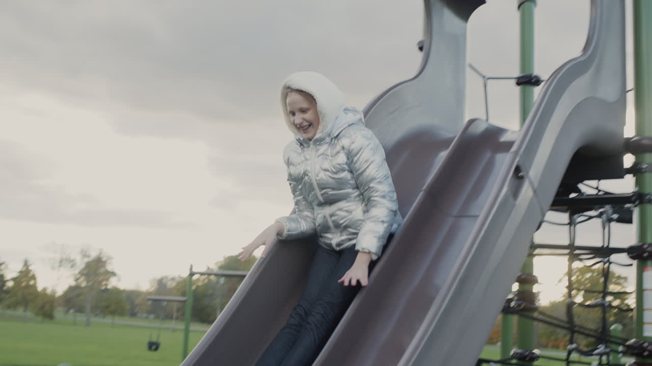 A ten-year-old girl slides down a children's slide on a playground in the park
