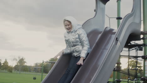 a ten-year-old girl slides down a children's slide on a playground in the park