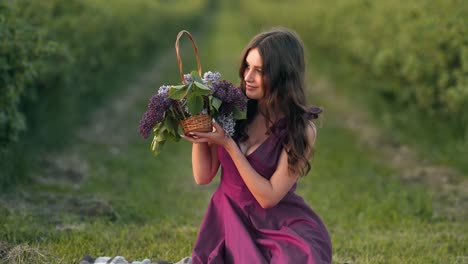 retrato de una hermosa joven en un campo con un vestido morado con una canasta de flores lilas