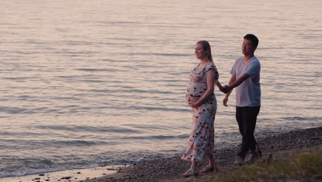 pareja multiétnica - hombre asiático y su esposa embarazada están caminando a lo largo de la orilla del mar